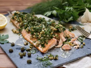 Lachs mit Kräuter-Walnuss-Salsa Angeschnittenes Lachsfilet mit Kräuter-Salsa, Kaper und Walnüsse auf Pergament