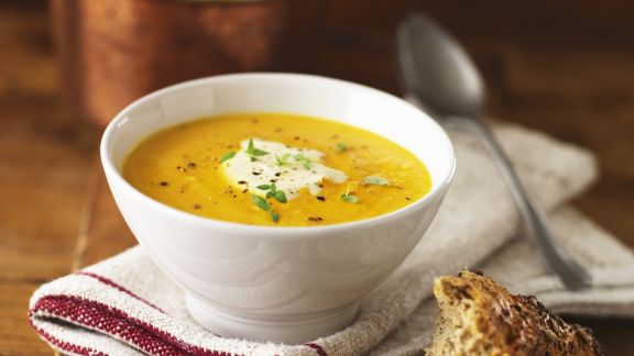 Orangefarbene Suppe in weißer Schale mit weißem Topping