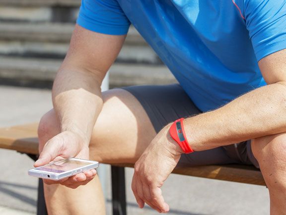 Mann in Sport-Outfit mit Mobiltelefon und Fitness-Tracker